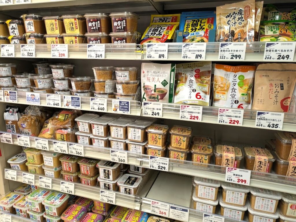 Various types of miso displayed on shelves in a Japanese supermarket.